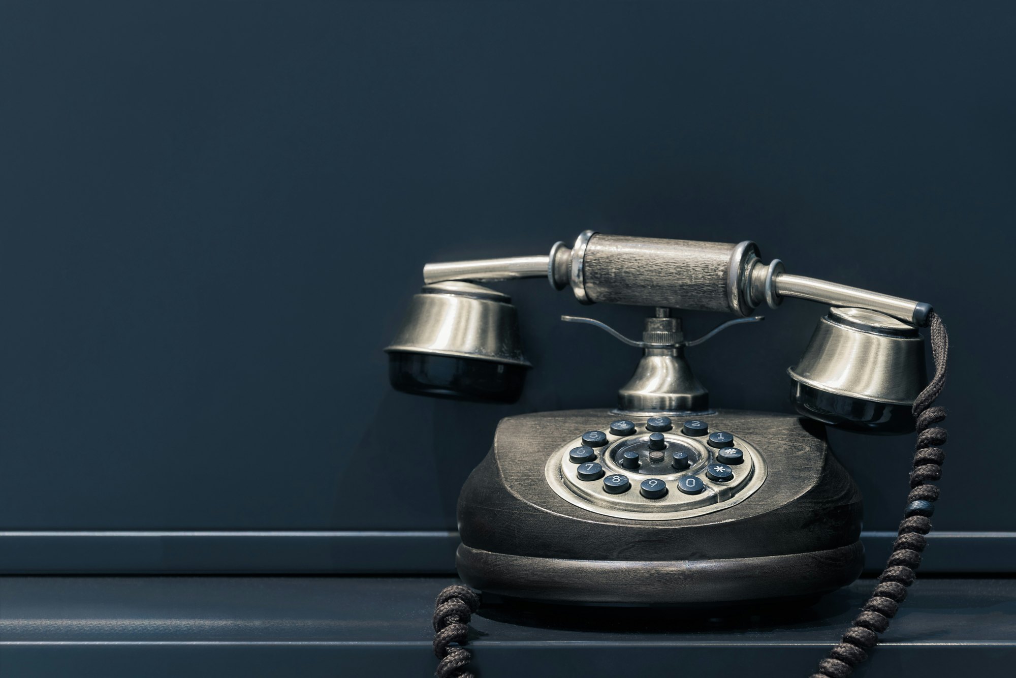 Een oude telefoon met kiesschijf tegen een donkerblauwe muur